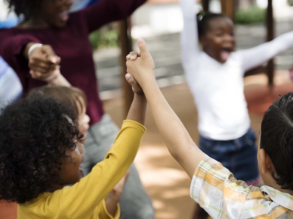 group of preschoolers on playground holding hands in a circle