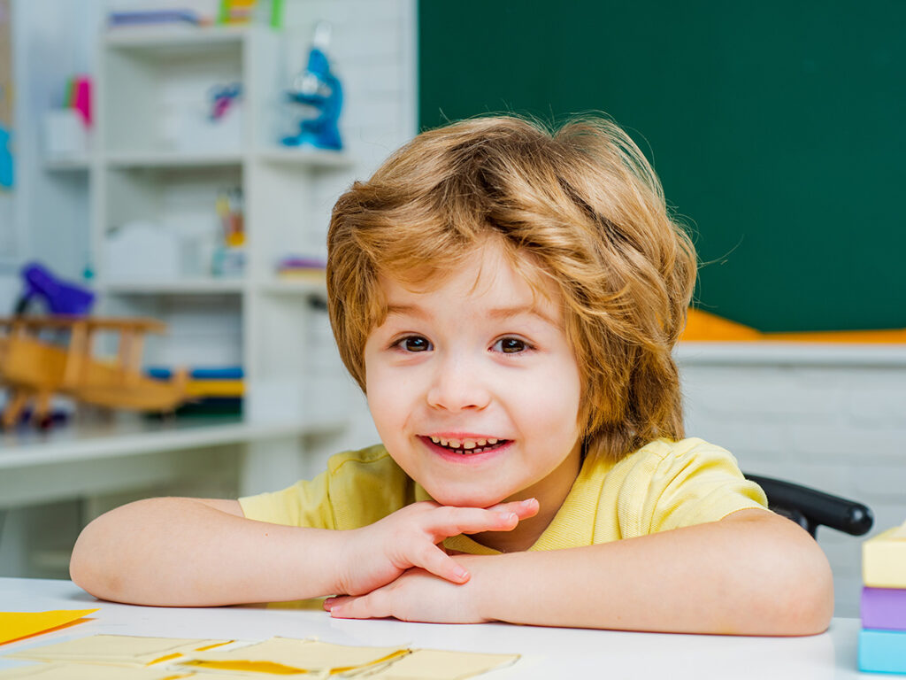 Happy, smiling boy sitting at a daycare center table.