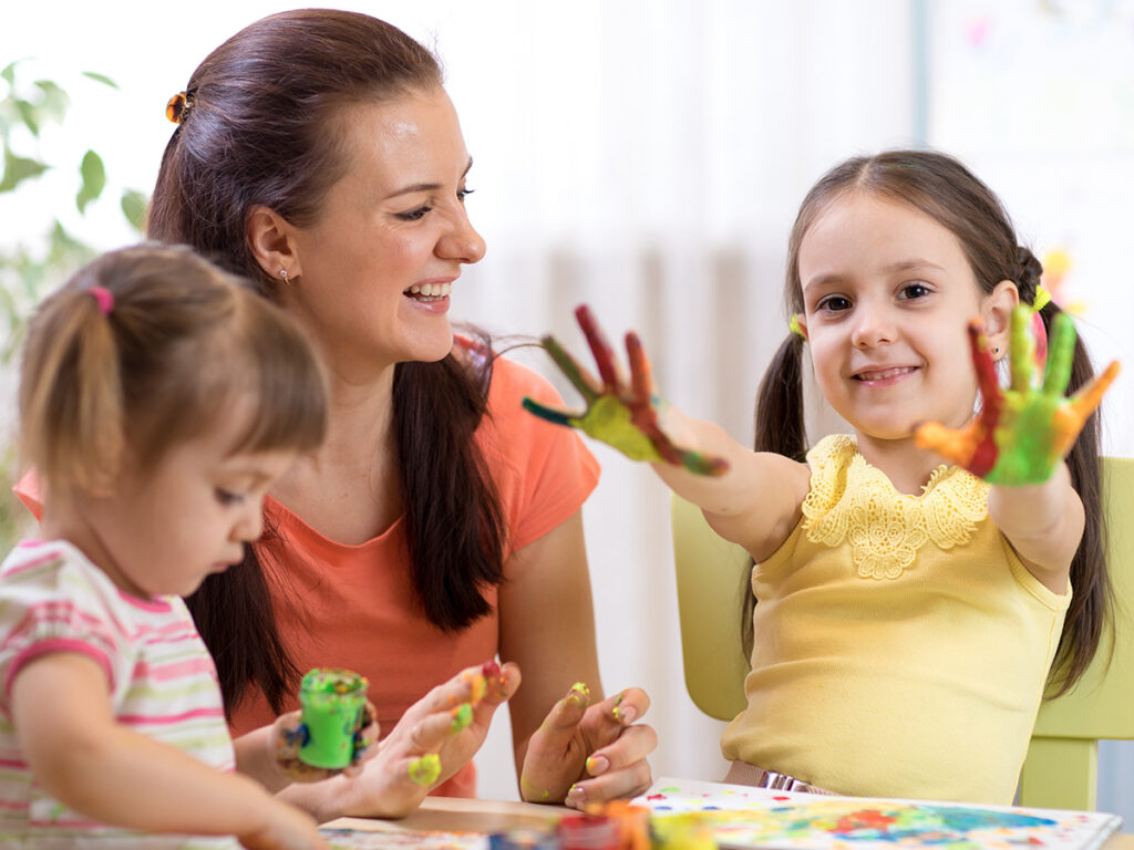 Child holds her hands out that are covered in fingerpaints from daycare center fingerpainting.