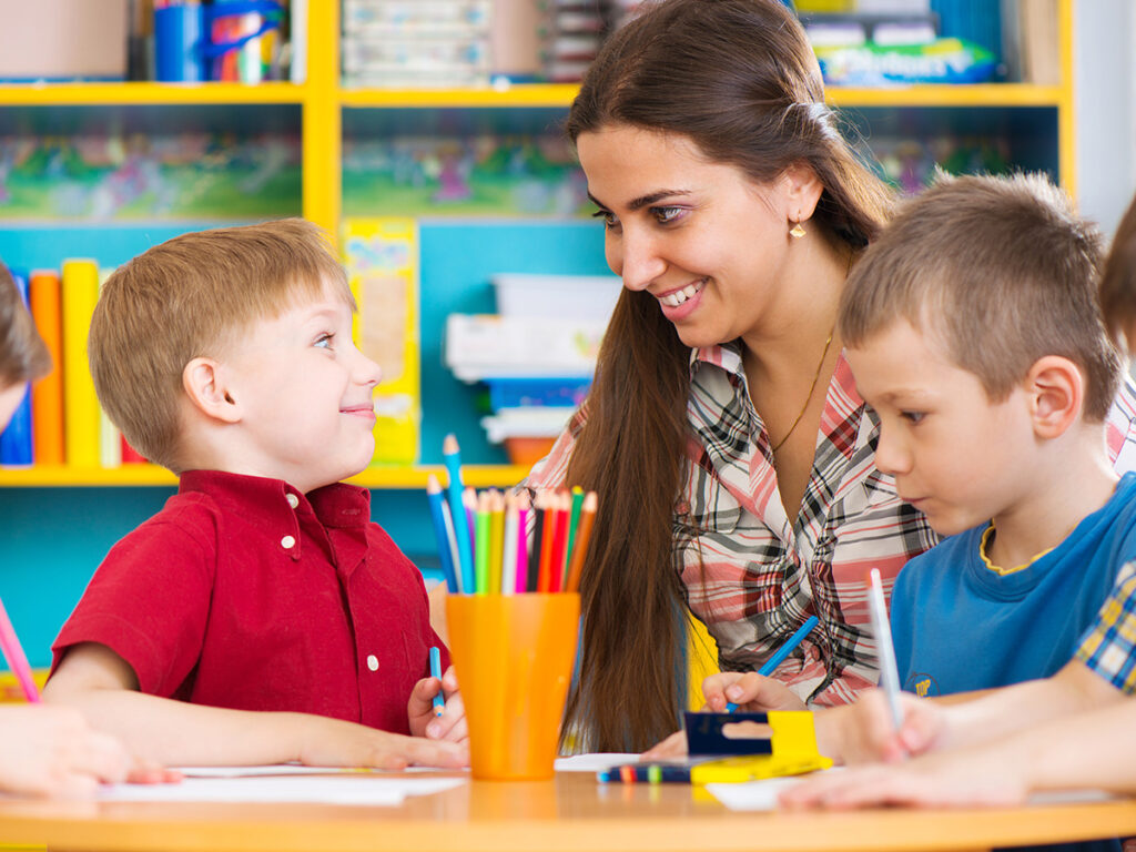 Teacher smiling while four children work on their activities.